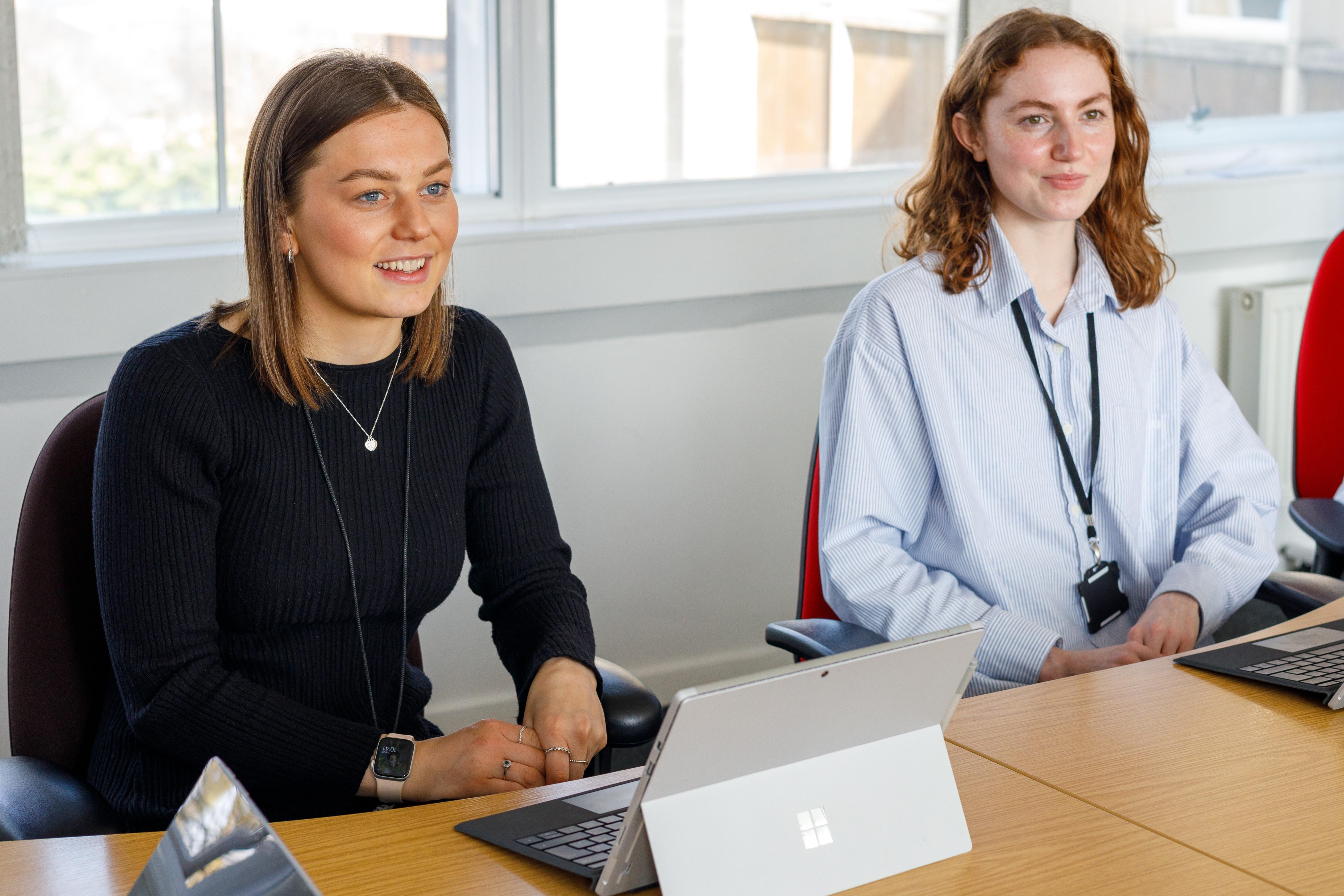 A picture of two new employees sat at a meeting desk