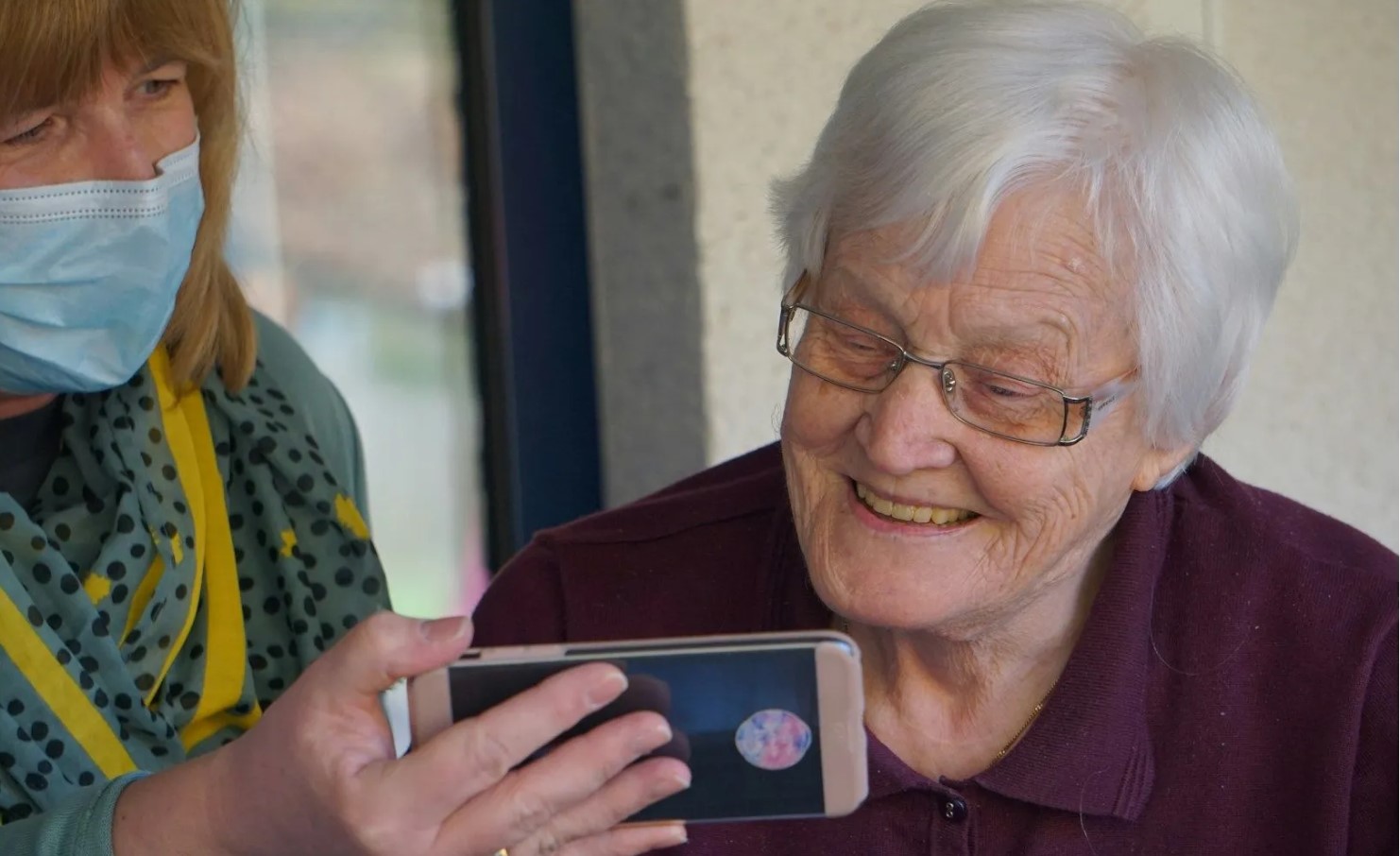 Care staff and care home resident smiling while looking at an image on a smartphone