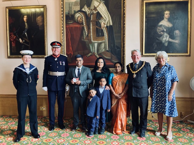 Aby Joseph (third from left) being presented with his British Empire Medal by Lord Lieutenant Tim Cox next to family and friends.