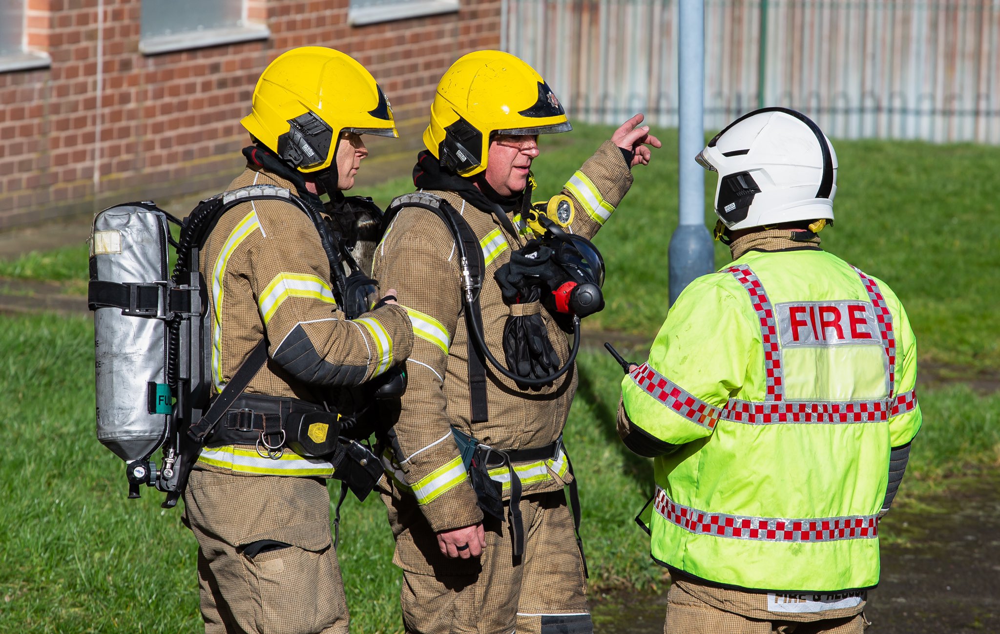Three firefighters stand outside building taking part in training exercise