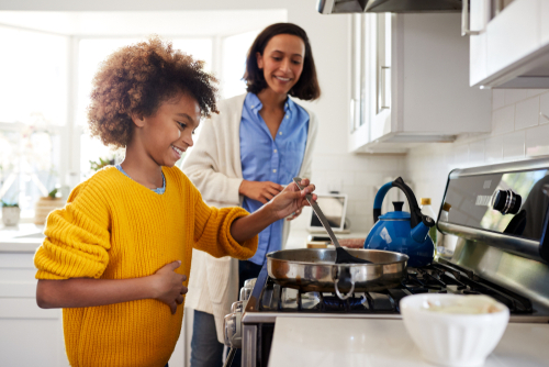 Child cooking on hob with parent supervising