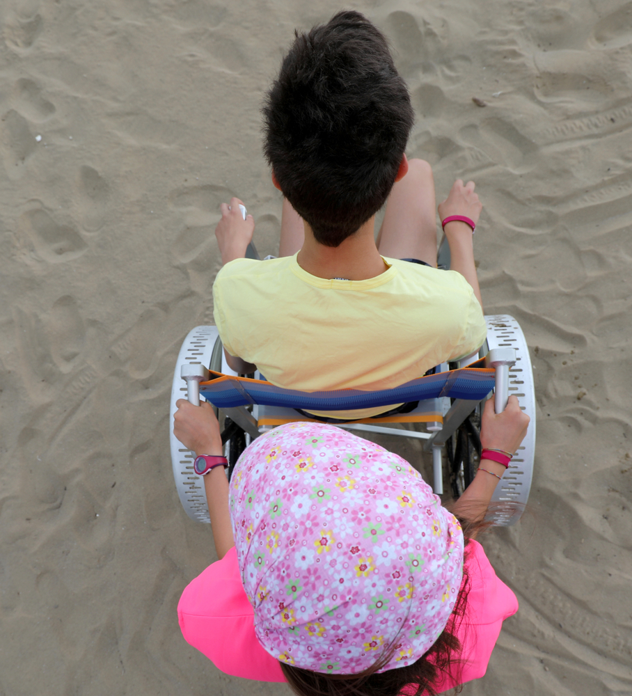 young girl pushes a boy in a wheelchair on a beach